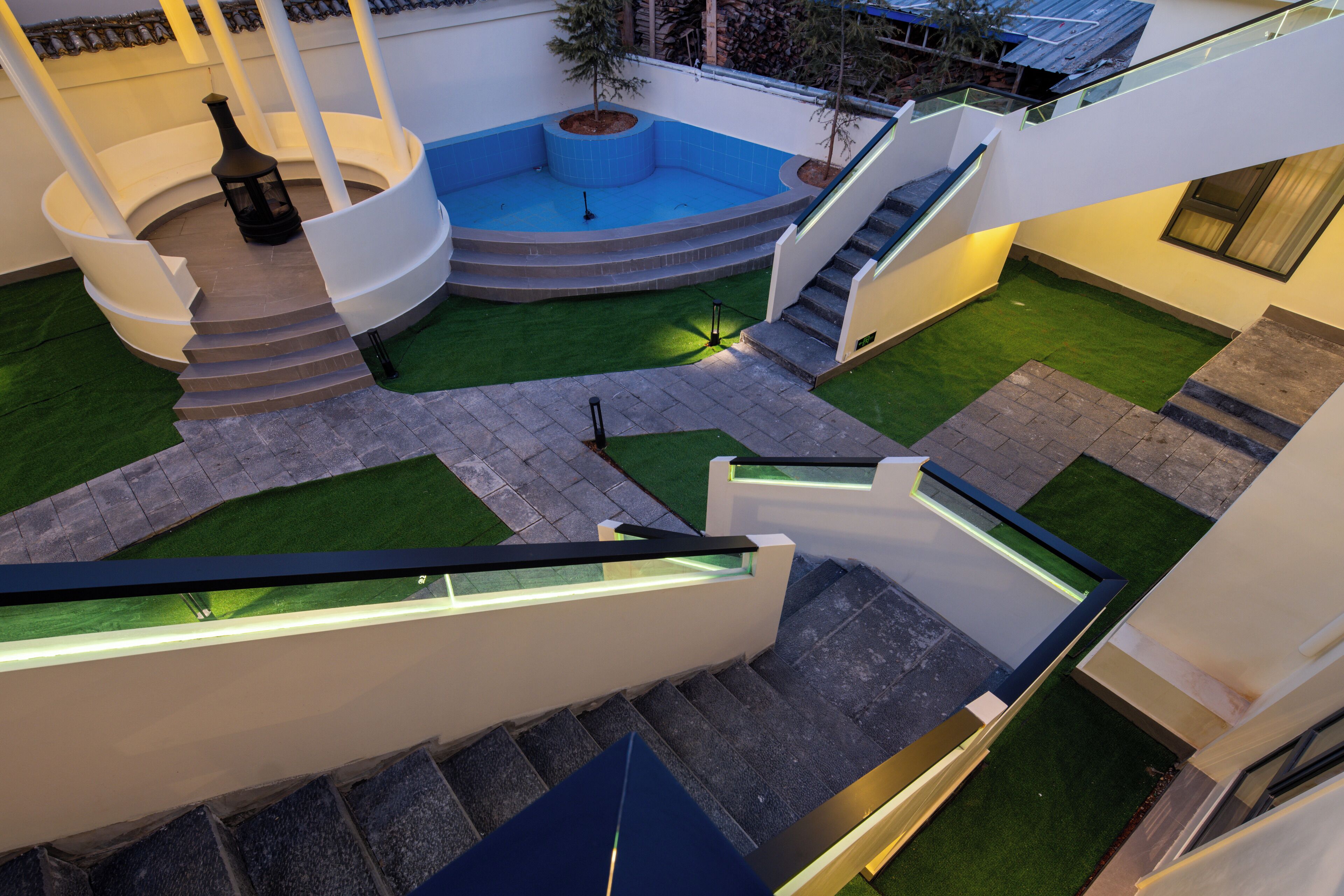 A modern outdoor area with a circular pool, steps leading to a lower level, and a small tree.