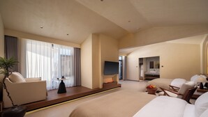 A hotel room with a large bed, a seating area with a table, a TV, and a bathroom with a sink and mirror. - Bandu Oxygen Supply Homestay (Deqin)