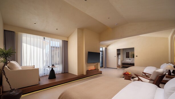 A hotel room with a large bed, a seating area with a table, a TV, and a bathroom with a sink and mirror. - Bandu Oxygen Supply Homestay (Deqin)