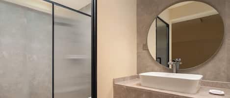 Un baño moderno con un espejo grande, un lavamanos rectangular y un separador de vidrio.