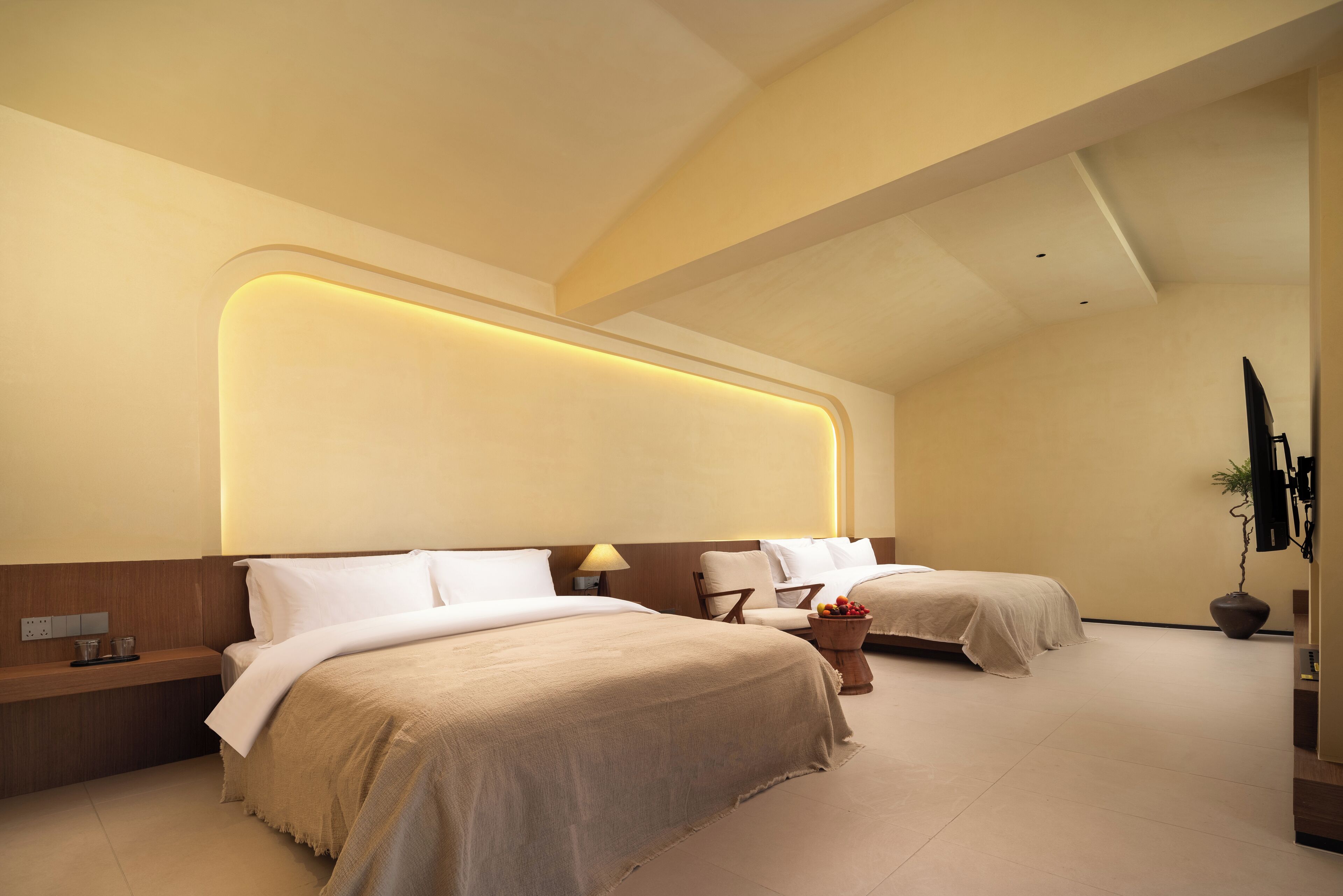 A modern hotel room with two beds, a bedside table, a lamp, and a potted plant.