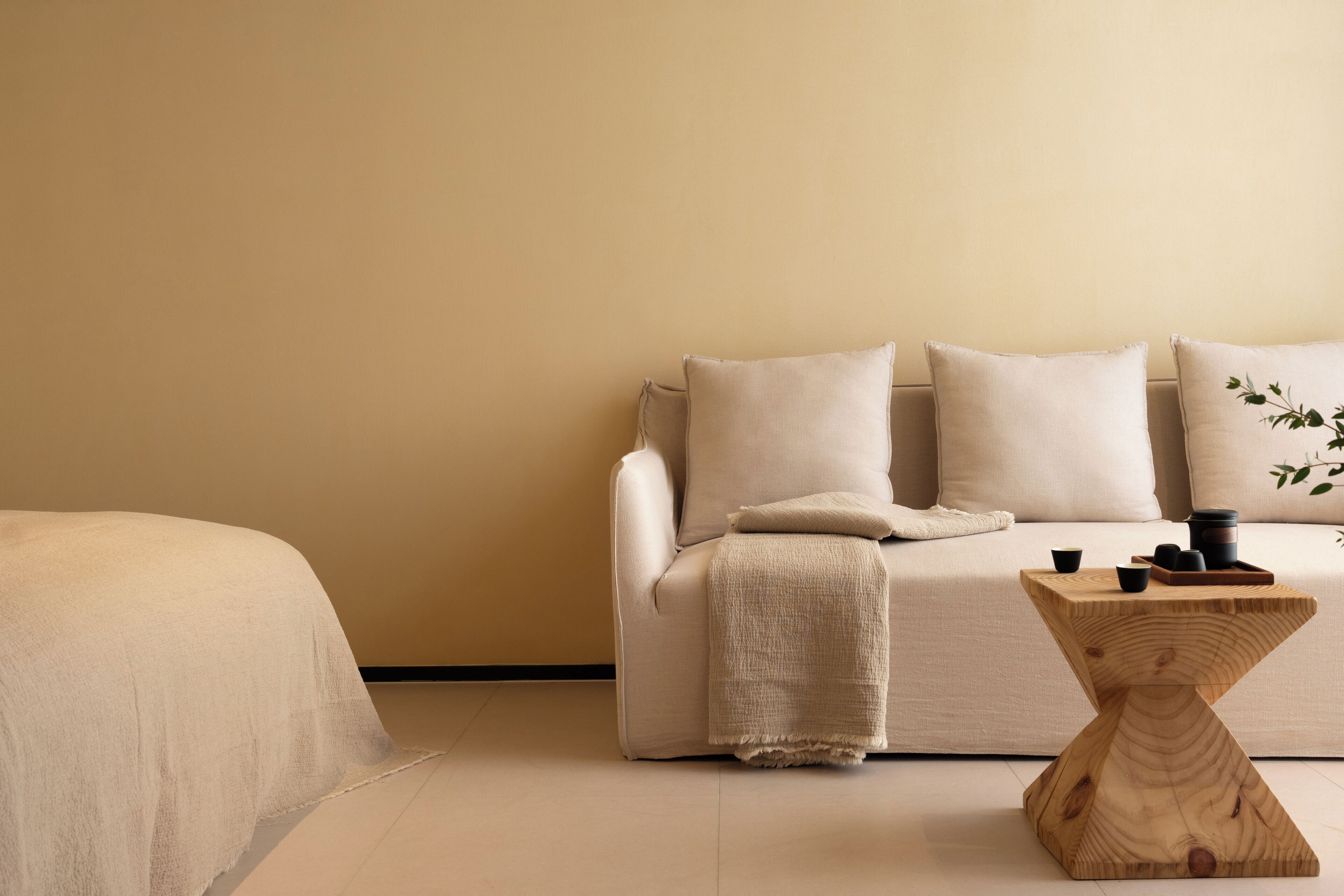 Een minimalistisch ingerichte kamer met een bank, een houten bijzettafeltje en een bed.