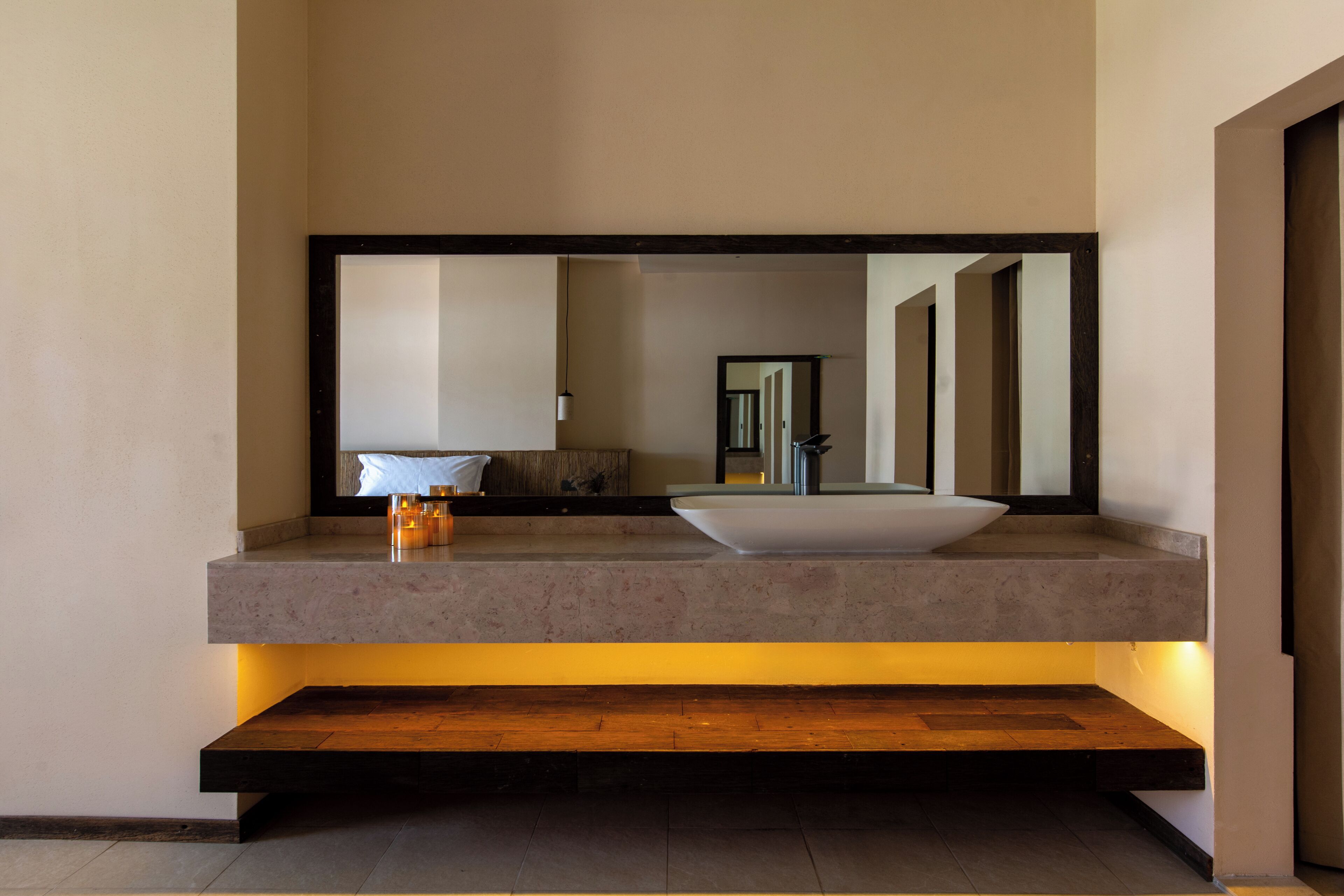 Une salle de bain moderne avec un grand miroir, un lavabo sur colonne et un banc en bois.