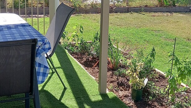 Un patio cubierto con mesa y sillas, rodeado de un césped cuidado y jardines.