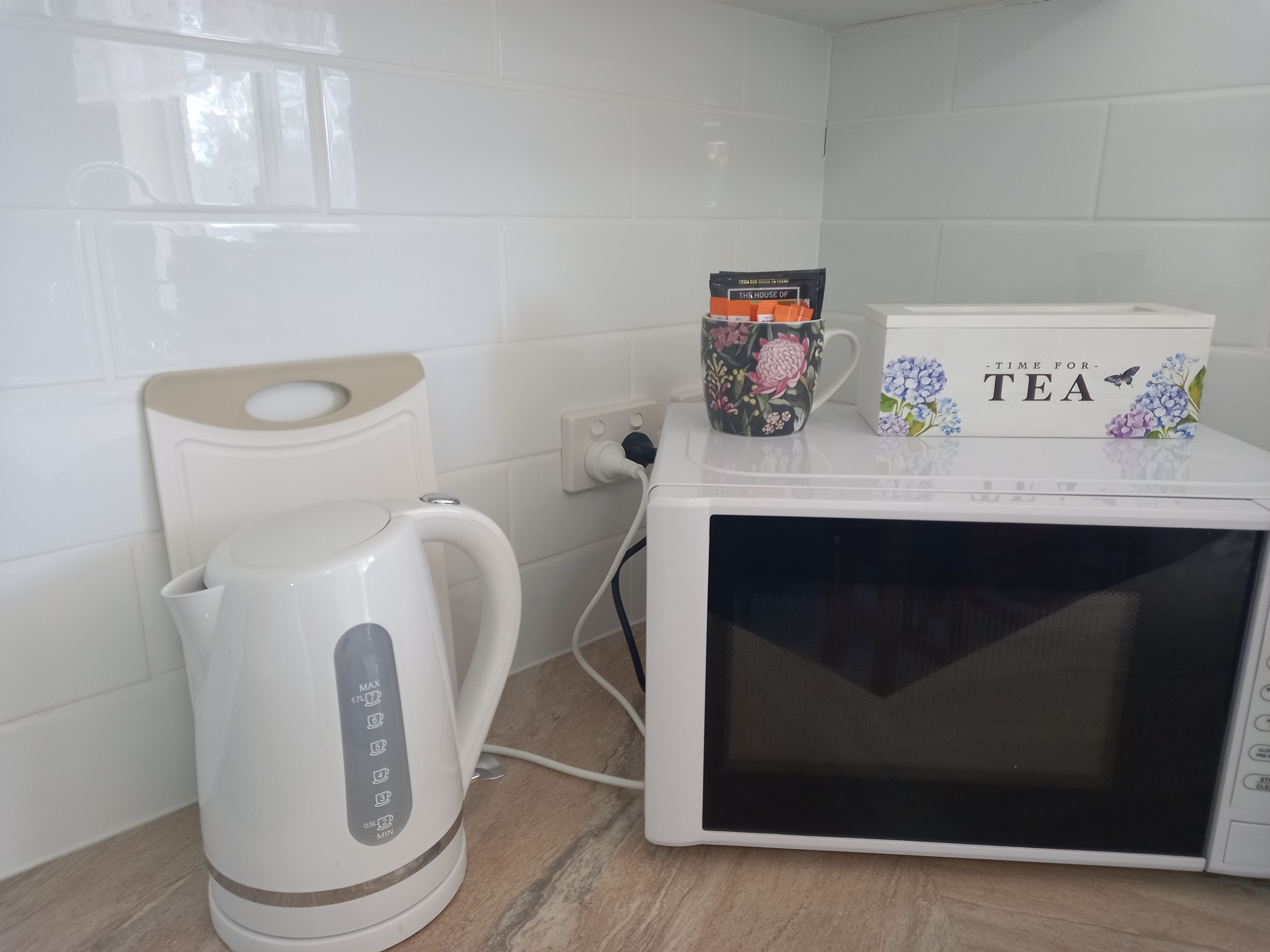 Een keuken met een witte waterkoker, een magnetron en een mok op het aanrecht.