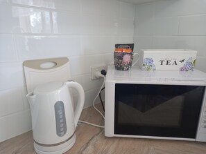 Una cocina con un hervidor blanco, un microondas y una taza en la encimera.