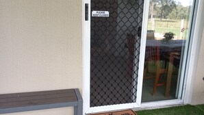 Een schuifdeur met horrengaas, een bord met de tekst 'Gesloten houden, alstublieft', een welkomstmat en een bankje buiten.