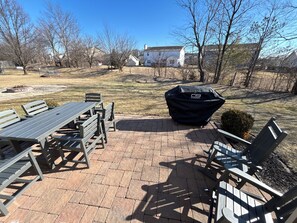 A patio with a table and chairs, a grill, and a brick pathway.