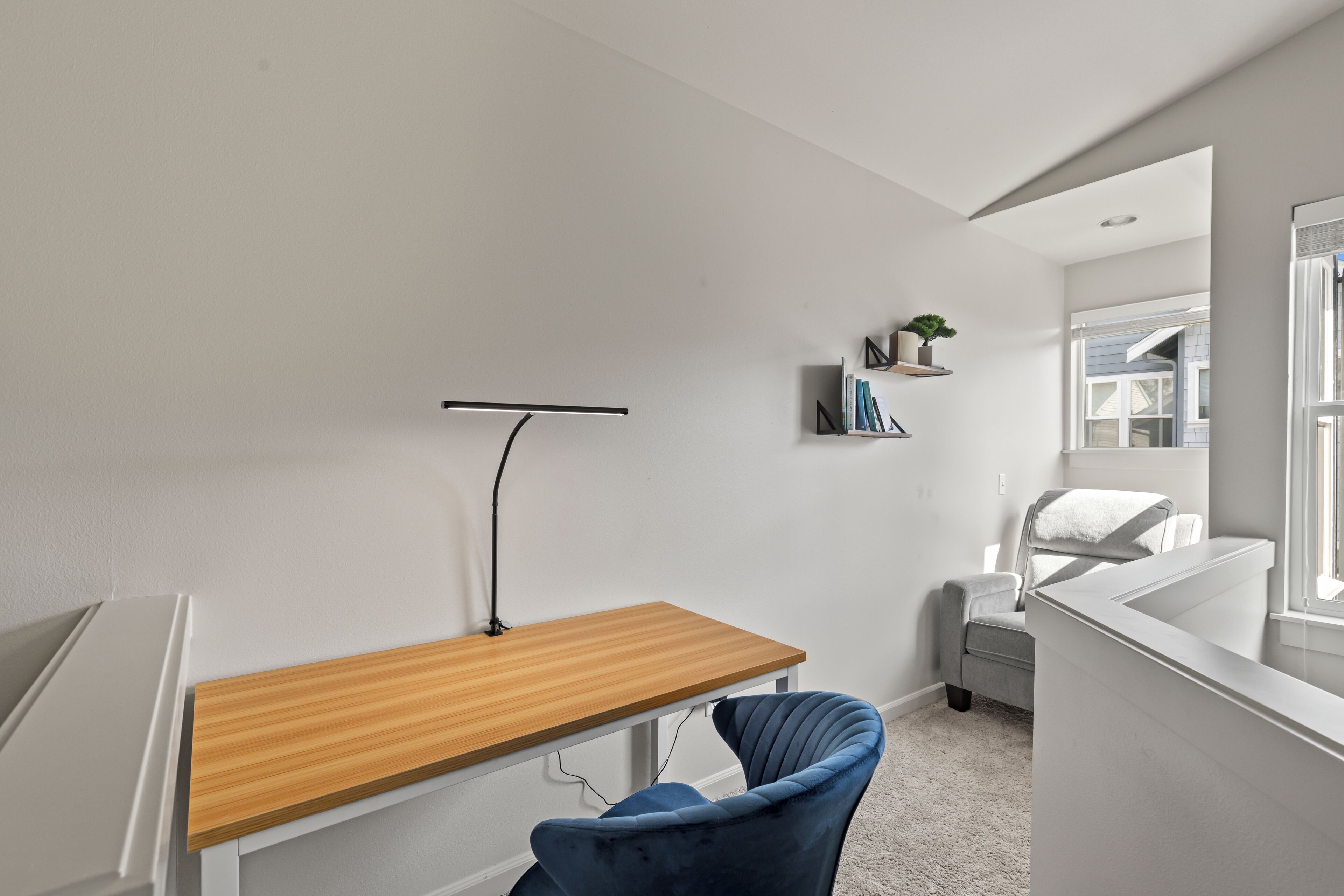 Et moderne værelse med et træskrivebord, en blå stol, en lille reol med bøger og et vindue.