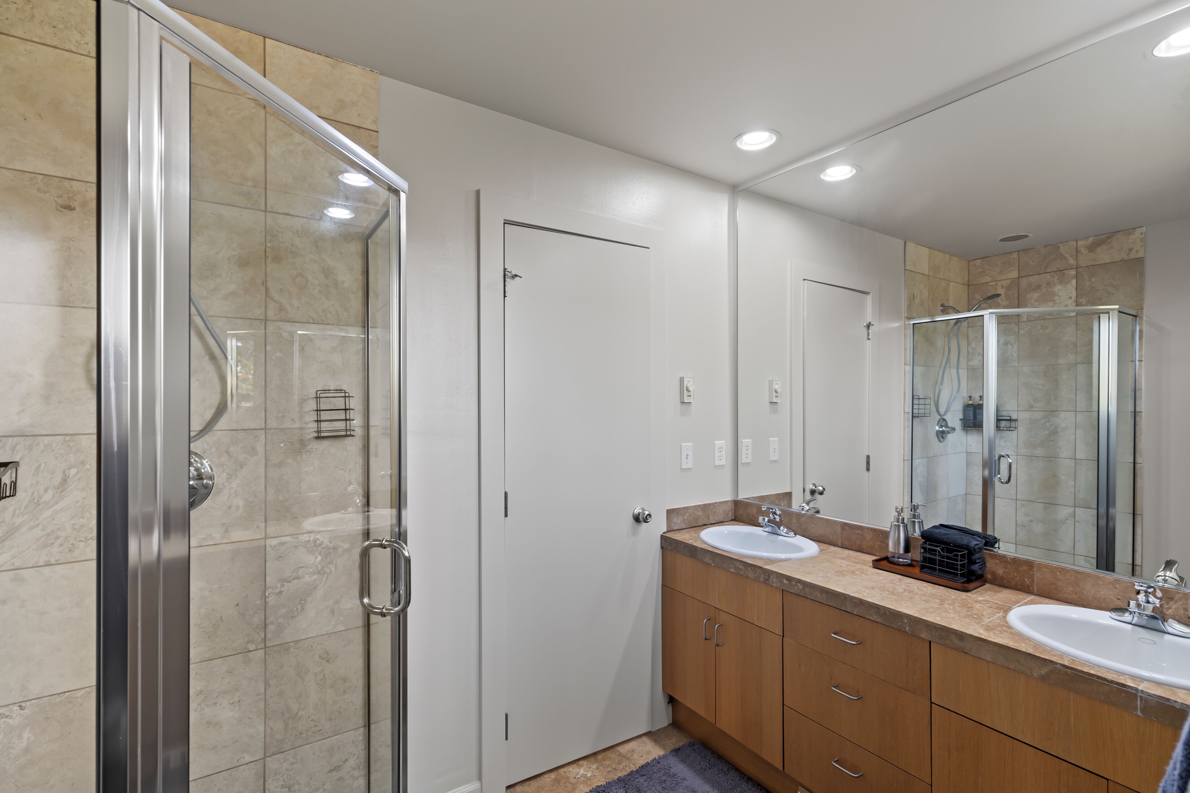 A modern bathroom with a glass shower enclosure, two sinks, a large mirror, and wooden cabinets.