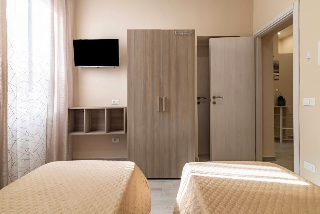 A bedroom with two beds, a wardrobe, a TV, and a shelf unit.