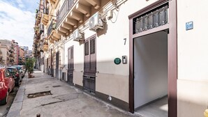 Une rue étroite en milieu urbain, bordée de voitures garées, et un immeuble dont l’entrée se trouve au rez-de-chaussée.