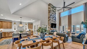 A spacious living area with a dining table, comfortable seating, a stone fireplace, and large windows offering a view.