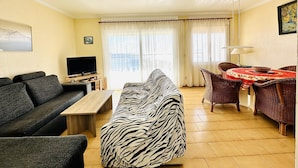 A living room with a sofa, a TV, a dining table with chairs, and a window with curtains. - 2210 - MIRADOR II 55 WONDERFUL SEA VIEW, IDEAL SITUATION FOR HIKING, 150m. FROM THE BEACH OR FROM THE ROCKS. (Roses)