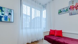 Ein Schlafzimmer mit einem Bett, einem Fenster mit transparenten Vorhängen und zwei an der Wand befestigten Kunstwerken.