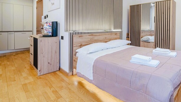Ein Schlafzimmer mit einem Bett, einem hölzernen Kopfteil, einem Kleiderschrank, einem Spiegel und einer Kaffeemaschine.