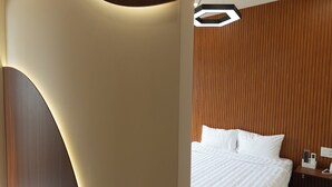 Una habitación de hotel moderna con un diseño de pared curva, un cabecero de madera, una cama bien hecha y una mesita de noche con una lámpara.