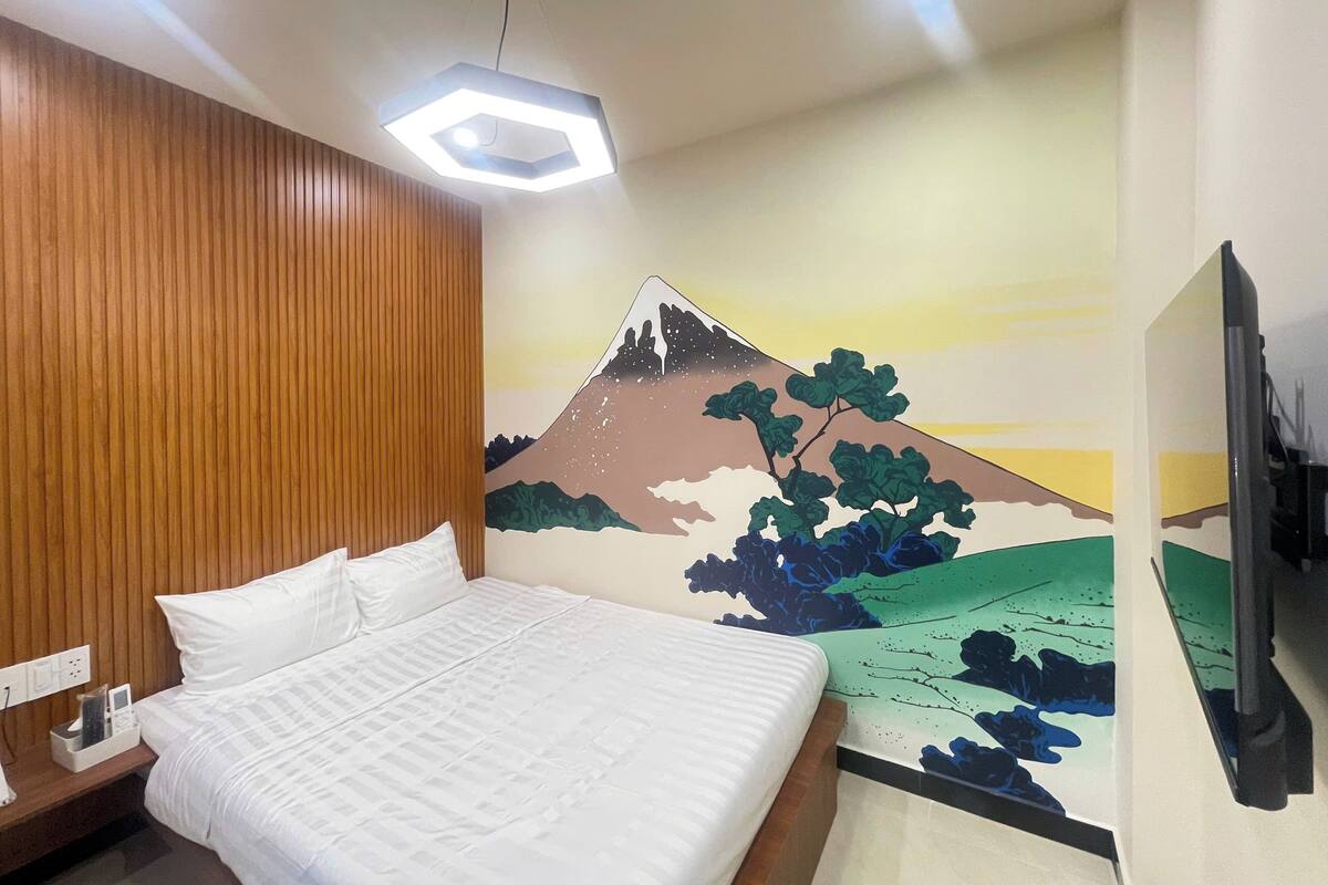 Une chambre d’hôtel avec un lit, un mur recouvert de panneaux en bois, un luminaire au plafond et une fresque murale représentant une montagne.