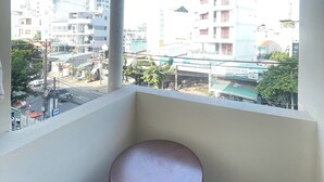 Un balcón con un taburete de madera, con vistas a un paisaje urbano con edificios y una calle.