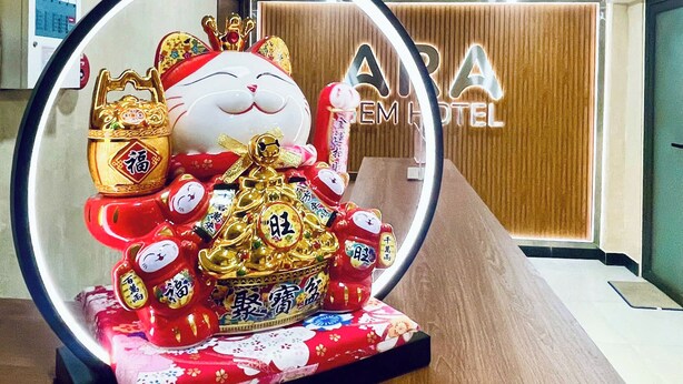 Una exhibición decorativa que presenta una gran figura de gato con varios adornos, sobre una superficie de madera en una habitación con una decoración de estilo moderno.