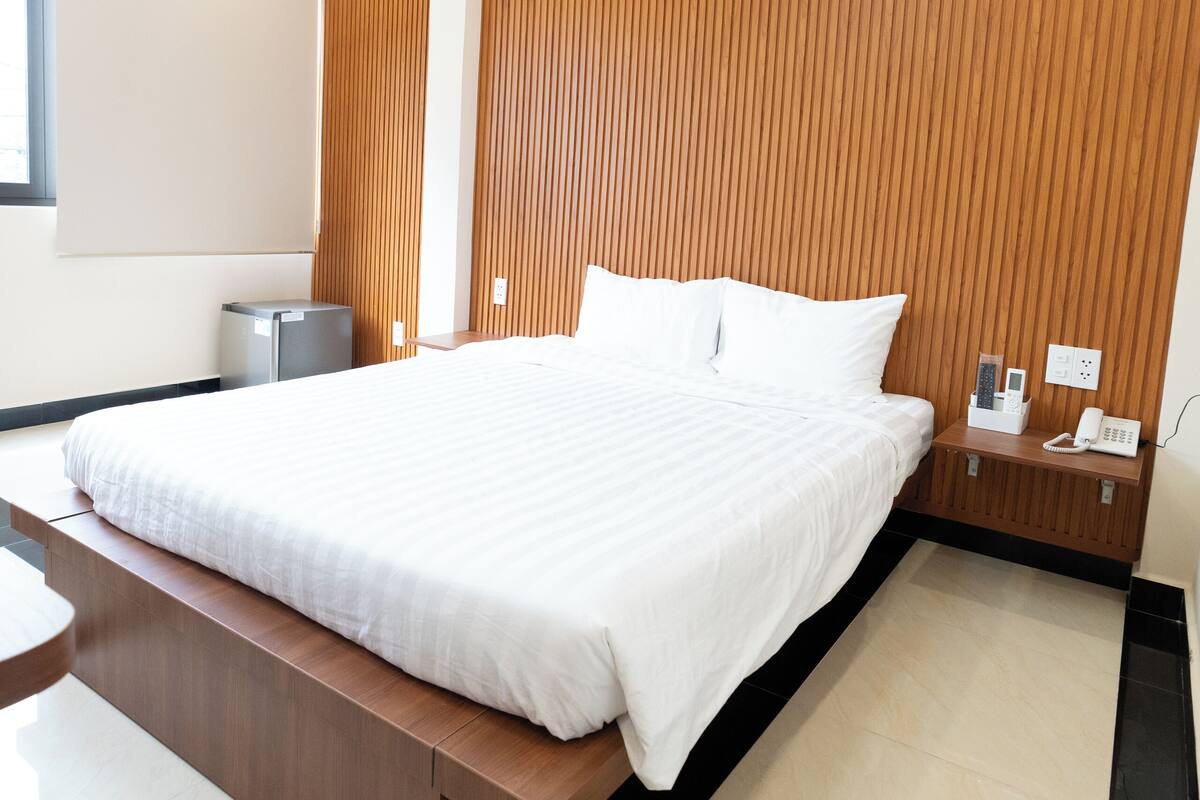 Une chambre d’hôtel moderne avec un grand lit, un mur revêtu de panneaux en bois et une petite table de chevet équipée d’un téléphone et d’un chargeur.