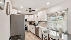 Una cocina moderna con armarios blancos, un refrigerador de acero inoxidable, lavavajillas, un fregadero y una ventana con persianas.