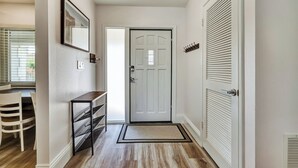 Un pasillo con una puerta blanca, un perchero, un escritorio con cajones y una silla.