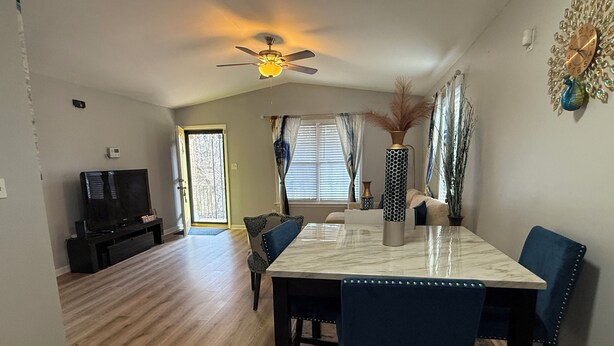 A dining area with a marble table, blue chairs, a ceiling fan, and a television in the background. - Blue Jay’s Nest
3bed/2bth, quick access to Hwy 29 (Greensboro)