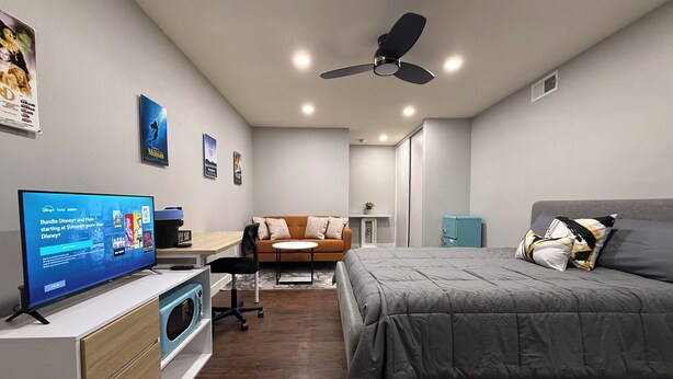 Ein modernes Schlafzimmer mit Bett, Schreibtisch, Stuhl, Fernseher und Deckenventilator.