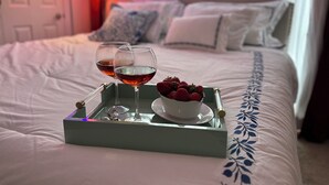 Een bed met een dienblad waarop twee glazen rode wijn, een schaal aardbeien en een witte kop staan.