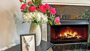 A fireplace with a fire, a vase with pink and white flowers, and a framed picture on a black table. - Last-Minute Chicago home with Rooftop Views +Private HOT TUB -Garage-Sleeps 12 (Chicago)