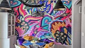 Een levendige kamer met een kleurrijke abstracte muurschildering, een eettafel met stoelen en hanglampen.