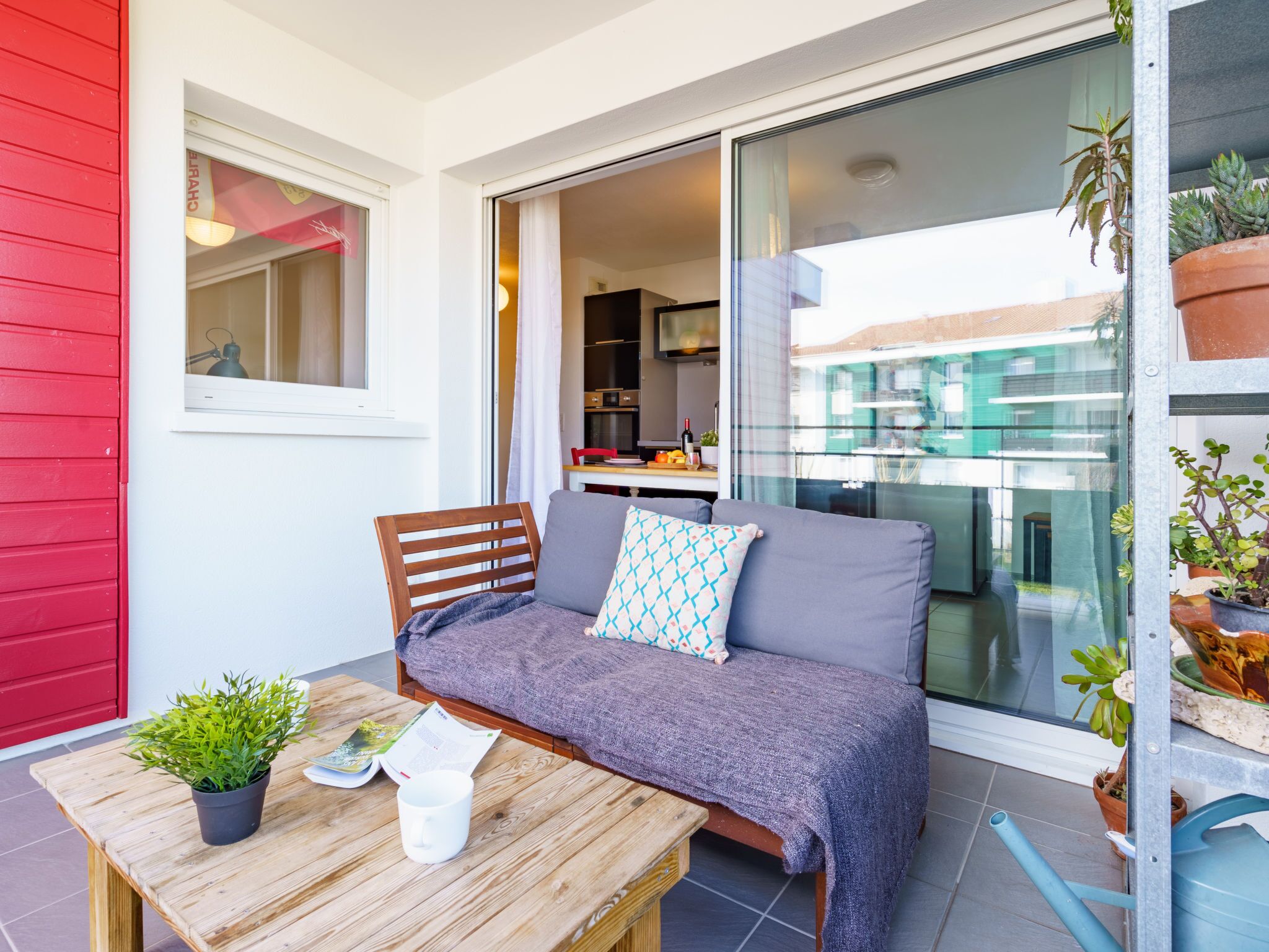 Ein Balkon mit einem Holztisch, einem grauen Sofa und einer roten Wand.