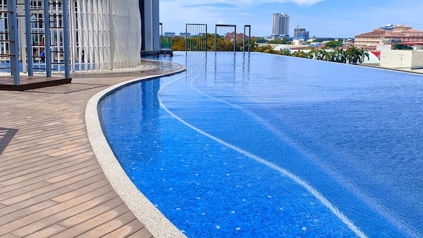 Una piscina con cubierta de madera, zona de estar techada y un paisaje urbano al fondo.