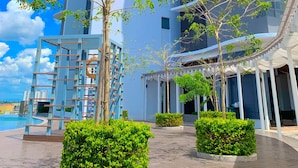 Un edificio moderno con varios balcones, una zona de piscina y vegetación bien cuidada.