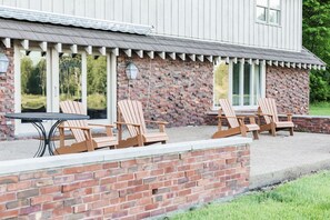 A building with a brick exterior and a covered patio area with Adirondack chairs and a table. - Hidden Gem in the Woods: Lost Creek Lodge (Terre Haute)