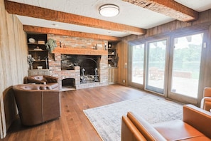 A living room with a brick fireplace, leather sofas, and a large sliding glass door leading to an outdoor area. - Hidden Gem in the Woods: Lost Creek Lodge (Terre Haute)