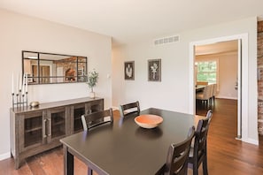 A dining area with a dark wooden table, chairs, and a large mirror above. There are framed pictures on the wall and a potted plant on the table. - Hidden Gem in the Woods: Lost Creek Lodge (Terre Haute)