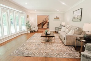 A spacious living room with a large window, a staircase, a sofa set, and a coffee table. - Hidden Gem in the Woods: Lost Creek Lodge (Terre Haute)