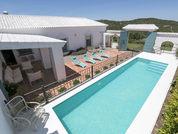 Una piscina con sillas de descanso, un espacio de patio y vistas del paisaje circundante.