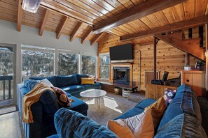 Interior acogedor de una cabaña de madera con un sofá azul grande, una chimenea y un televisor.