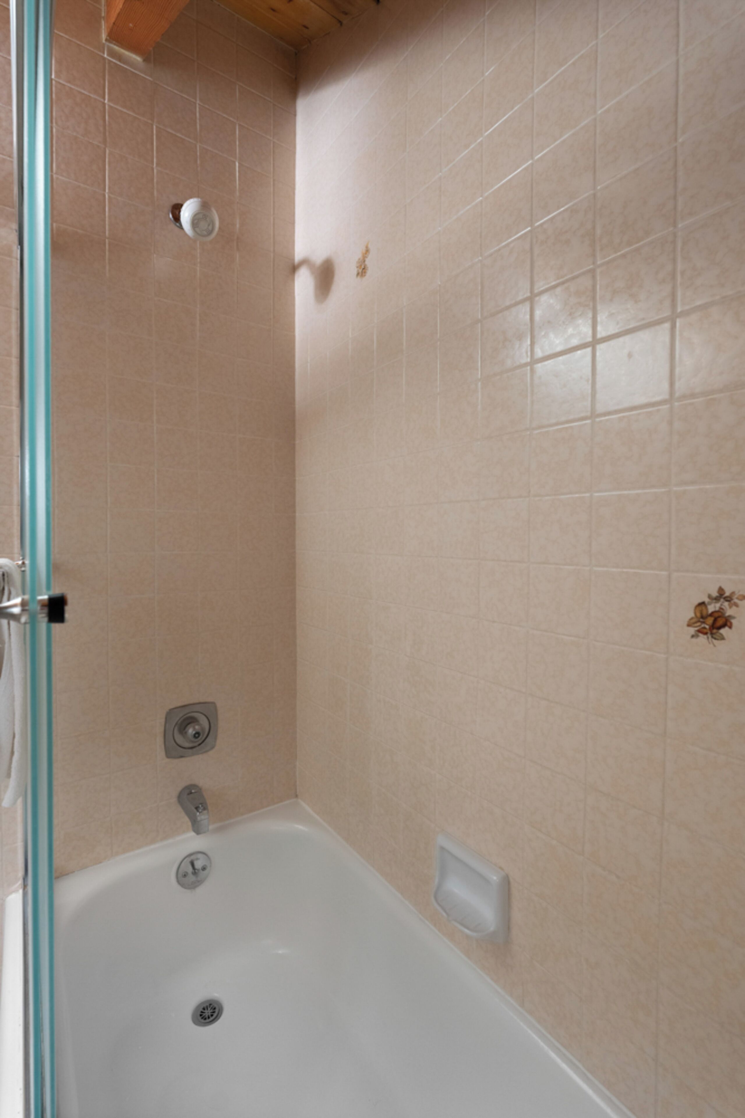 A bathroom with a bathtub, a glass shower enclosure, and beige tiled walls.