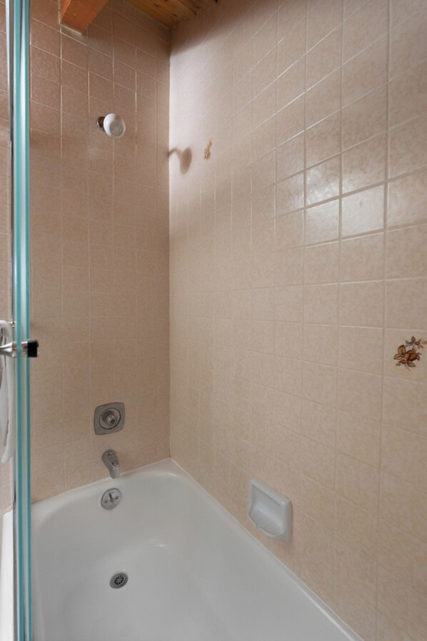 Un baño con bañera, cabina de ducha de vidrio y paredes de cerámica color beige.