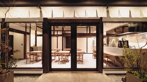 A traditional Japanese-style interior with tatami mat flooring, wooden furniture, and a view of the adjacent kitchen area. - HAPPOYA (Hachinohe)