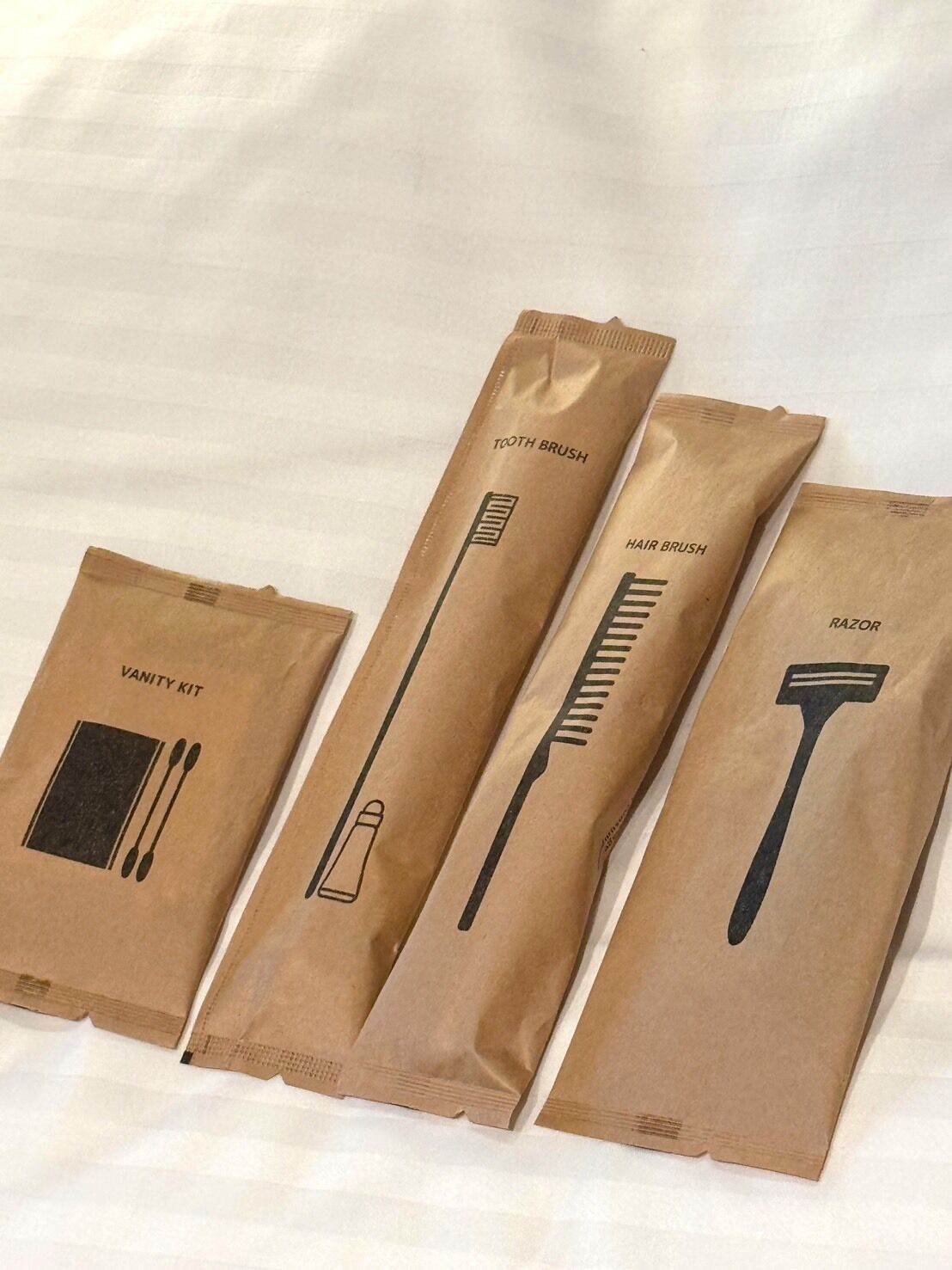 Four brown paper bags with different grooming tools labeled: 'TOOTH BRUSH,' 'HAIR BRUSH,' 'VANITY KIT,' and 'RAZOR.'