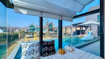 A modern room with a large window overlooking a swimming pool and a view of houses.