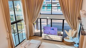 A modern living room with a large window, a sofa, a dining table set for four, and a flat-screen TV.