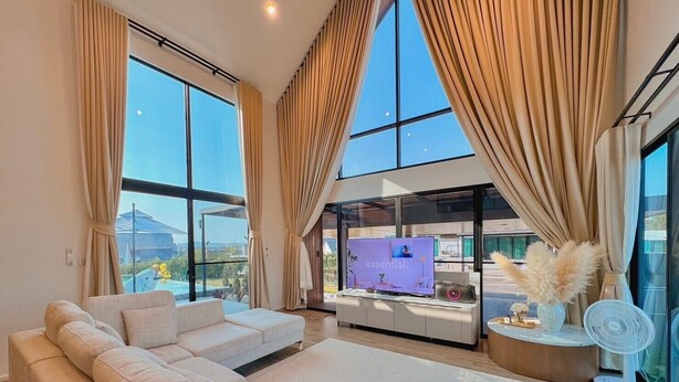 A spacious living room with a large sectional sofa, a flat-screen TV, and a view of a swimming pool and mountains.
