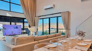 A modern dining area with a large window, beige curtains, and a table set for a meal.