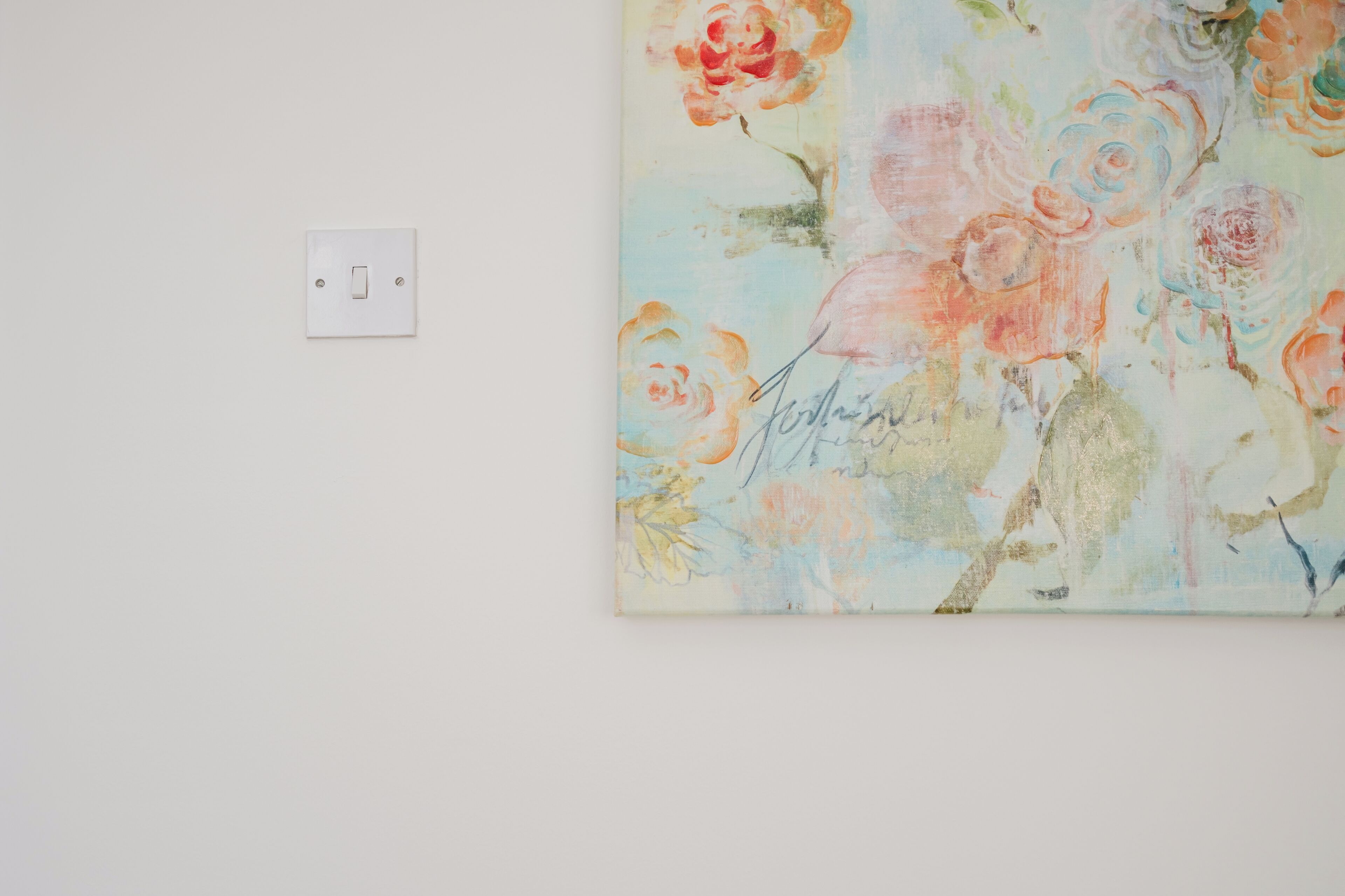 A wall with a single light switch and a large floral painting.